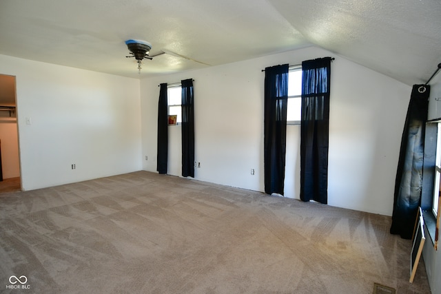 unfurnished bedroom with a textured ceiling, vaulted ceiling, light colored carpet, and ceiling fan