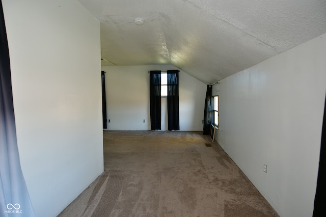 unfurnished room featuring lofted ceiling, a textured ceiling, and light colored carpet