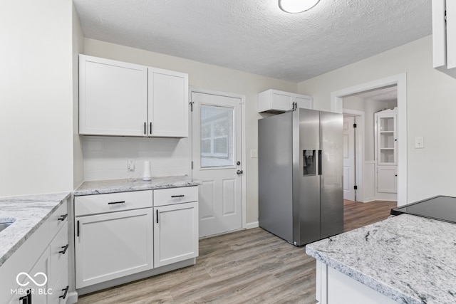 kitchen with white cabinets, light hardwood / wood-style floors, a textured ceiling, and stainless steel fridge