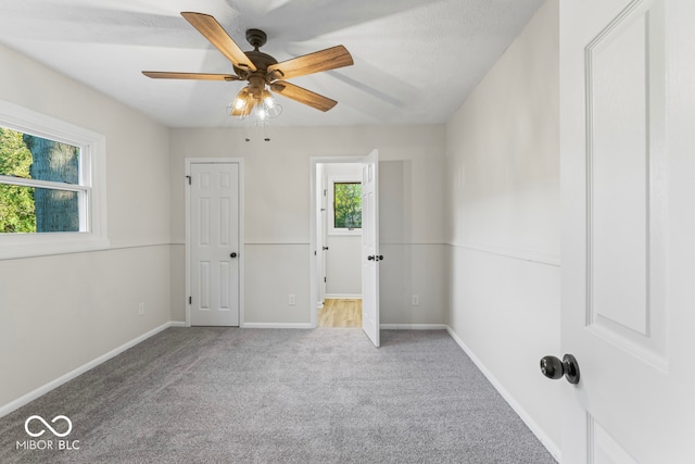 carpeted empty room featuring a textured ceiling, ceiling fan, and a wealth of natural light