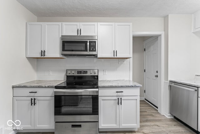 kitchen featuring light hardwood / wood-style floors, white cabinetry, stainless steel appliances, and light stone counters