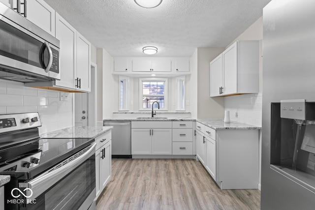 kitchen featuring light stone countertops, appliances with stainless steel finishes, sink, light hardwood / wood-style floors, and white cabinets