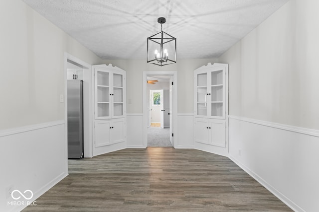 unfurnished dining area with a chandelier, a textured ceiling, and dark hardwood / wood-style flooring