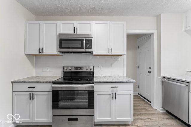 kitchen featuring white cabinets, backsplash, appliances with stainless steel finishes, light stone countertops, and light hardwood / wood-style floors