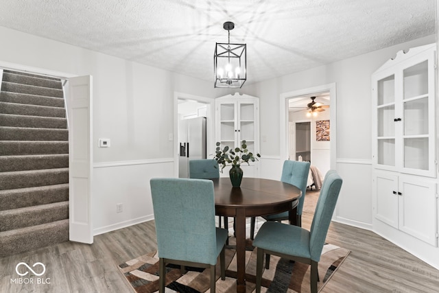 dining area with hardwood / wood-style floors, a textured ceiling, and ceiling fan with notable chandelier