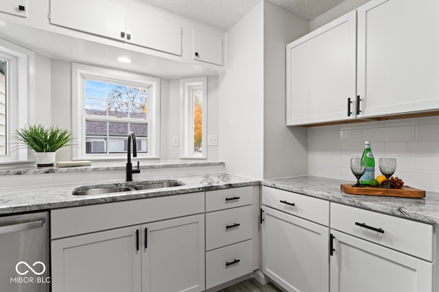 kitchen featuring decorative backsplash, dishwasher, sink, white cabinets, and a textured ceiling