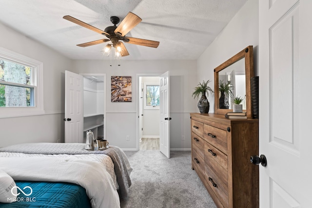 carpeted bedroom with a walk in closet, a textured ceiling, and ceiling fan