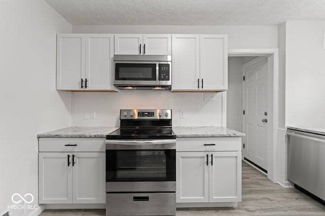 kitchen with decorative backsplash, white cabinetry, appliances with stainless steel finishes, light stone counters, and light hardwood / wood-style floors