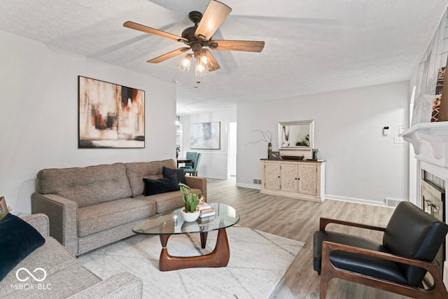 living room featuring a fireplace, a textured ceiling, light wood-type flooring, and ceiling fan