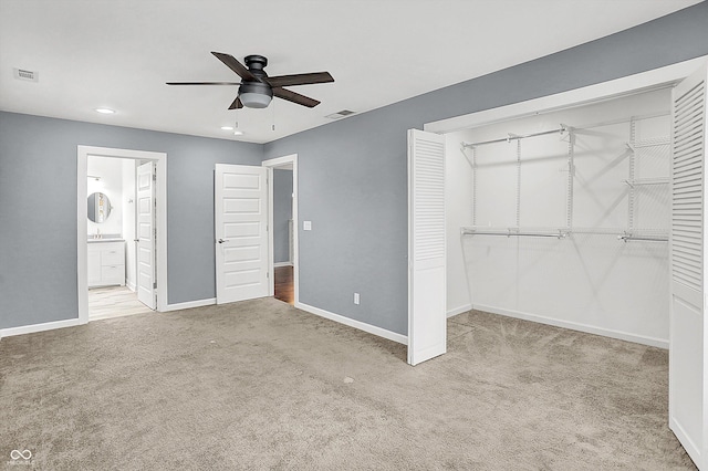 unfurnished bedroom with ceiling fan, light colored carpet, a closet, and ensuite bath