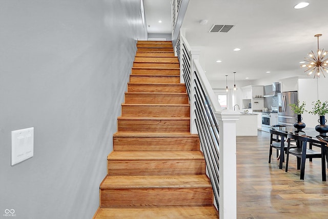 stairway featuring sink, wood-type flooring, and a notable chandelier