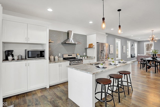 kitchen featuring white cabinets, stainless steel appliances, wall chimney exhaust hood, and an island with sink