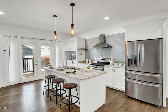 kitchen featuring white cabinets, wall chimney exhaust hood, stainless steel appliances, and a center island with sink