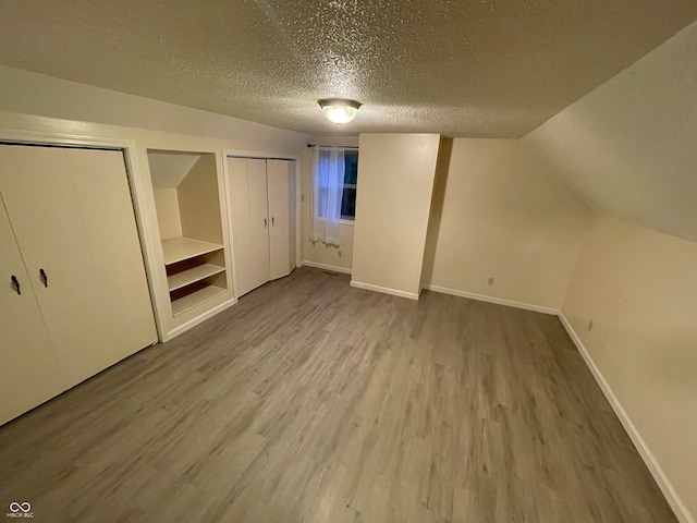 additional living space featuring a textured ceiling, hardwood / wood-style flooring, and vaulted ceiling