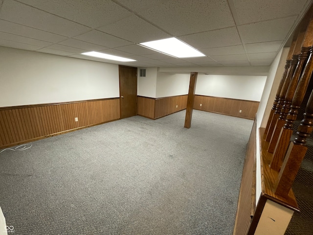 basement with a paneled ceiling, wood walls, and light colored carpet