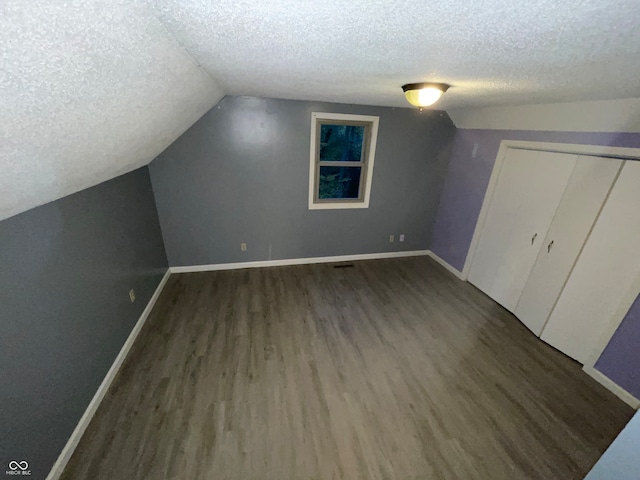 additional living space featuring dark hardwood / wood-style floors, a textured ceiling, and vaulted ceiling