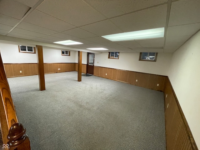 basement with wood walls, a paneled ceiling, and carpet flooring