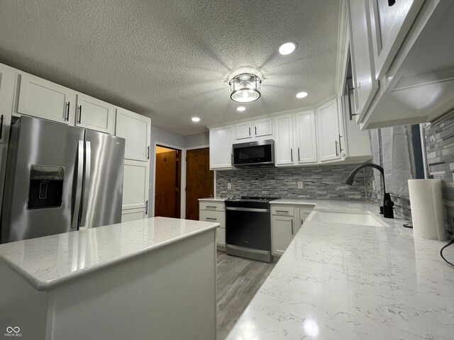 kitchen featuring sink, white cabinets, appliances with stainless steel finishes, a textured ceiling, and light hardwood / wood-style floors