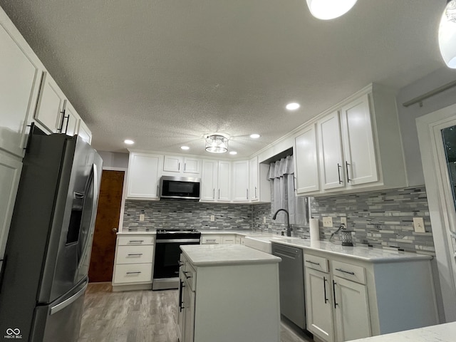 kitchen with a kitchen island, stainless steel appliances, sink, white cabinets, and light hardwood / wood-style floors