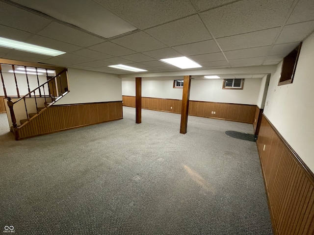 basement featuring a drop ceiling, carpet floors, and wood walls