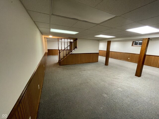 basement featuring a drop ceiling, wood walls, and carpet