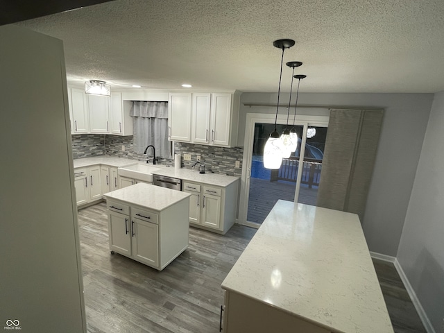 kitchen with a kitchen island, hanging light fixtures, white cabinetry, stainless steel dishwasher, and hardwood / wood-style flooring