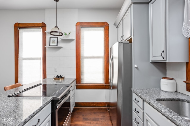 kitchen featuring decorative backsplash, dark wood-type flooring, stainless steel appliances, light stone countertops, and pendant lighting