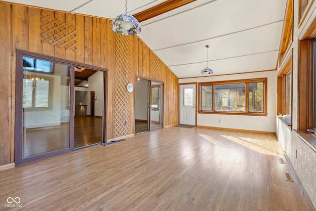 unfurnished living room featuring a wealth of natural light, hardwood / wood-style floors, high vaulted ceiling, and wooden walls