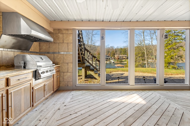 interior space with light hardwood / wood-style floors, a healthy amount of sunlight, a water view, and wall chimney range hood