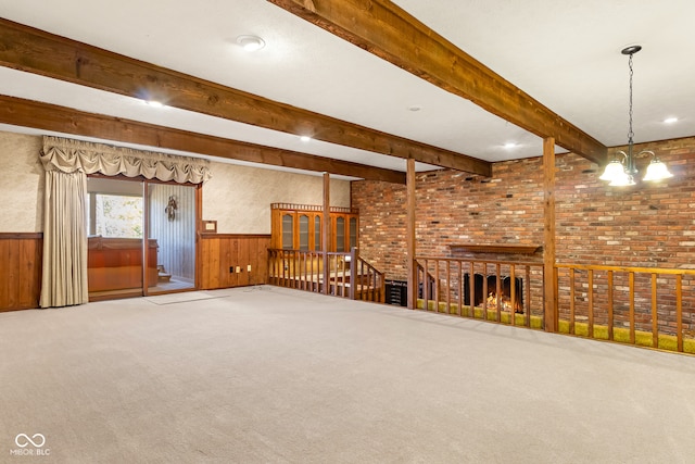 unfurnished living room featuring carpet, wood walls, beam ceiling, brick wall, and a chandelier