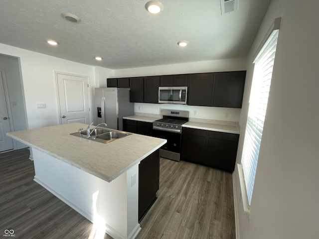 kitchen with hardwood / wood-style flooring, a center island with sink, appliances with stainless steel finishes, a textured ceiling, and sink