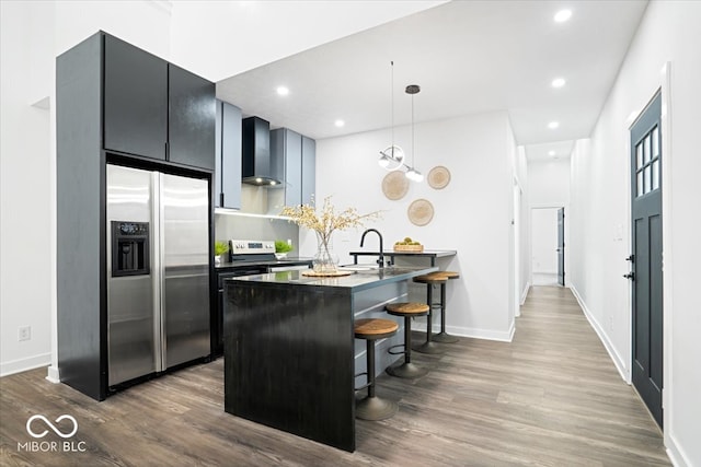 kitchen with wall chimney exhaust hood, a kitchen breakfast bar, kitchen peninsula, decorative light fixtures, and appliances with stainless steel finishes