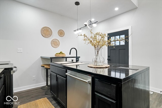 kitchen featuring an island with sink, stainless steel dishwasher, dark wood-type flooring, sink, and decorative light fixtures