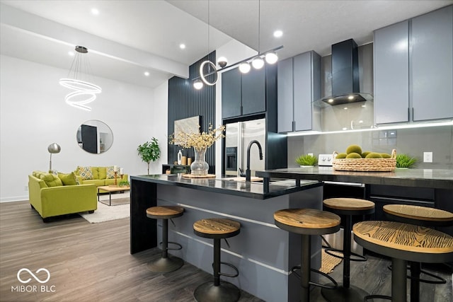 kitchen featuring wall chimney exhaust hood, a kitchen bar, decorative light fixtures, and hardwood / wood-style flooring