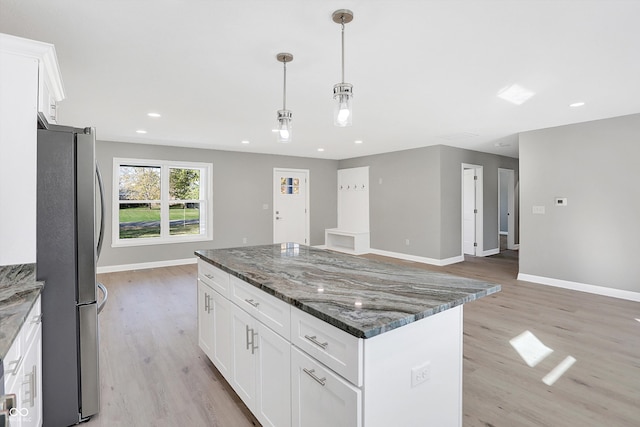 kitchen featuring stainless steel fridge, white cabinets, light wood-type flooring, dark stone counters, and a center island