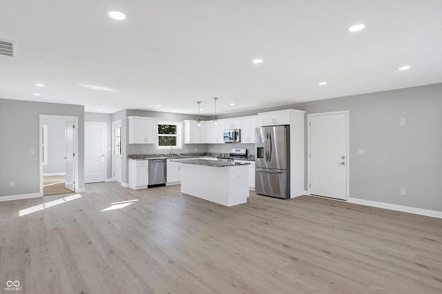 kitchen with appliances with stainless steel finishes, a kitchen island, hanging light fixtures, white cabinetry, and light hardwood / wood-style floors