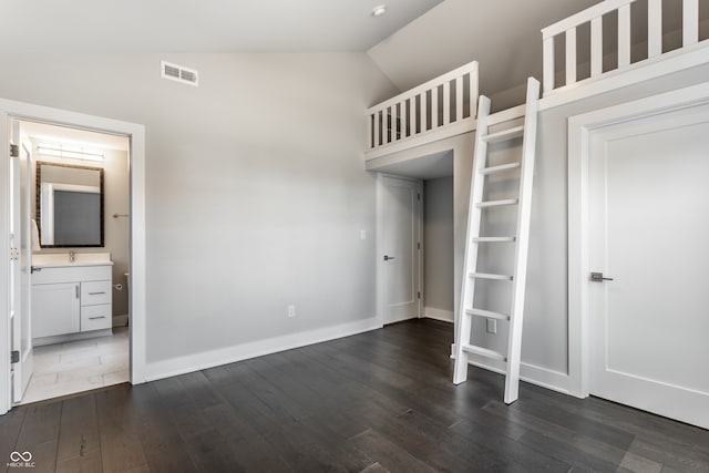 unfurnished bedroom featuring lofted ceiling, dark wood-type flooring, and connected bathroom