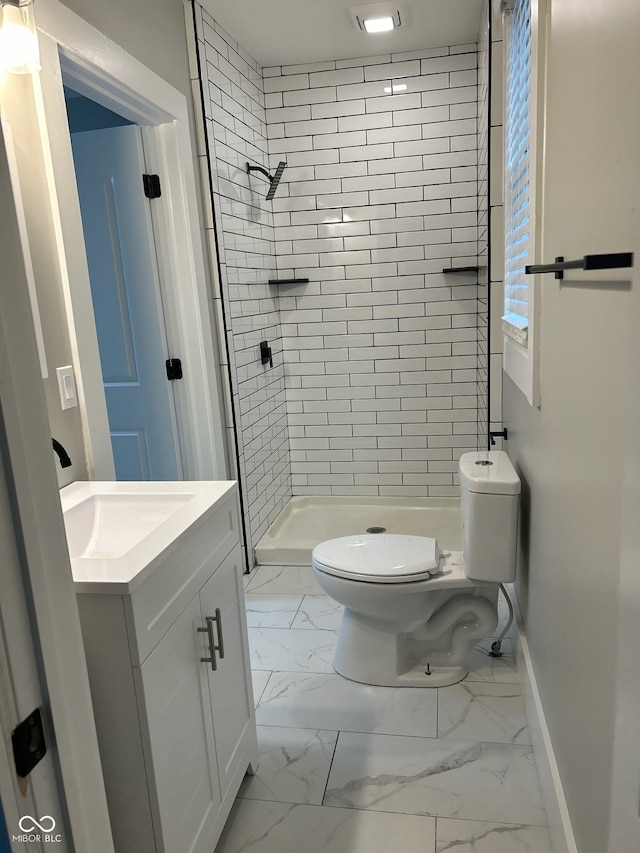 bathroom with a tile shower, toilet, and vanity