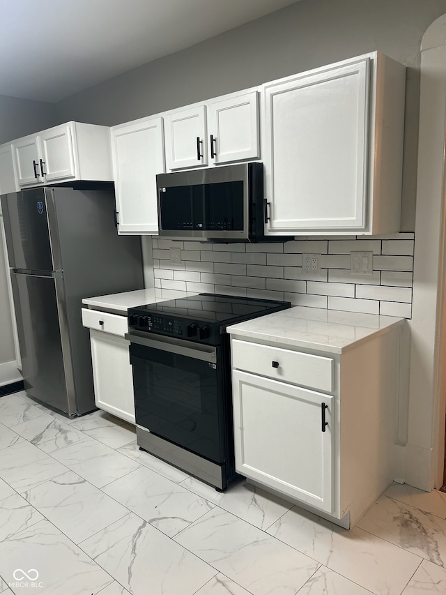 kitchen featuring white cabinetry, light stone counters, stainless steel appliances, and backsplash