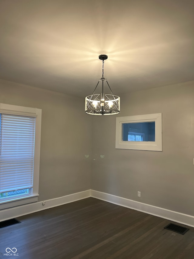 spare room featuring dark wood-type flooring and a notable chandelier