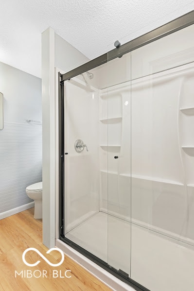 bathroom with toilet, hardwood / wood-style flooring, walk in shower, and a textured ceiling