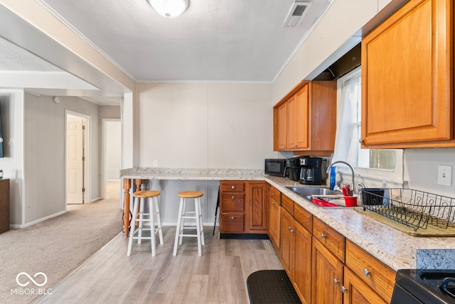 kitchen featuring crown molding, sink, light wood-type flooring, and a kitchen breakfast bar