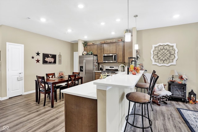 kitchen with appliances with stainless steel finishes, a kitchen bar, light wood-type flooring, kitchen peninsula, and pendant lighting