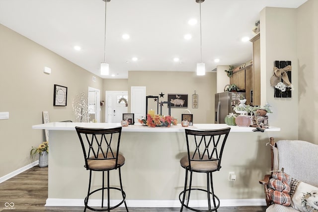 kitchen featuring a breakfast bar area, stainless steel fridge, hanging light fixtures, and dark hardwood / wood-style floors