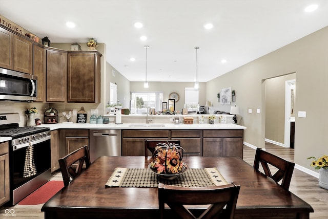 kitchen with stainless steel appliances, dark brown cabinets, sink, decorative light fixtures, and light hardwood / wood-style floors