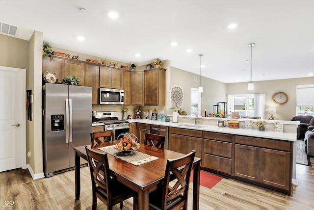 kitchen with hanging light fixtures, kitchen peninsula, sink, appliances with stainless steel finishes, and light hardwood / wood-style floors