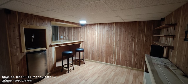 bar featuring a paneled ceiling, wood walls, and light hardwood / wood-style floors