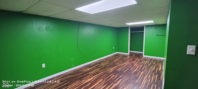 basement featuring a paneled ceiling and dark hardwood / wood-style floors