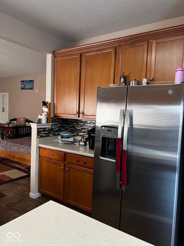 kitchen with stainless steel refrigerator with ice dispenser, dark tile patterned flooring, backsplash, and a textured ceiling