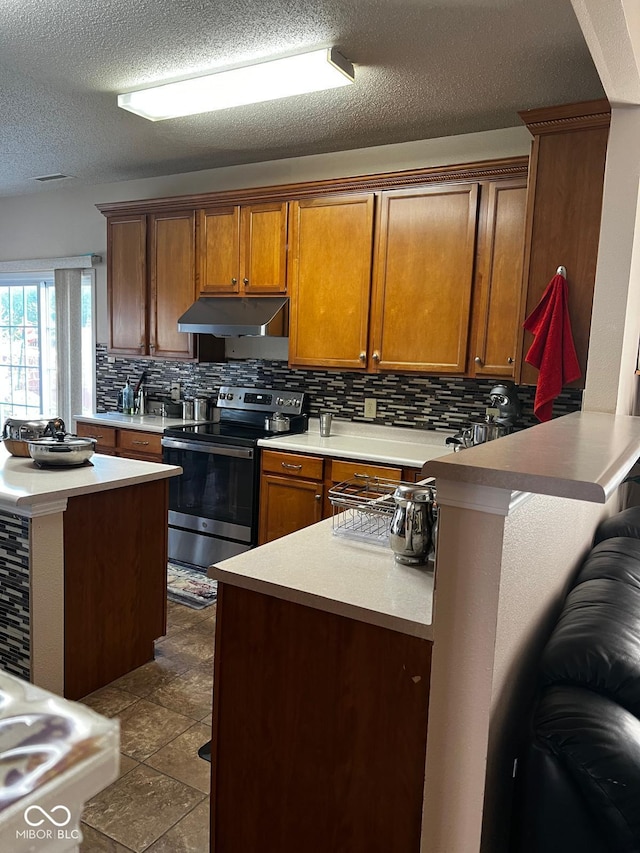 kitchen with decorative backsplash, kitchen peninsula, tile patterned flooring, a breakfast bar area, and stainless steel range with electric stovetop